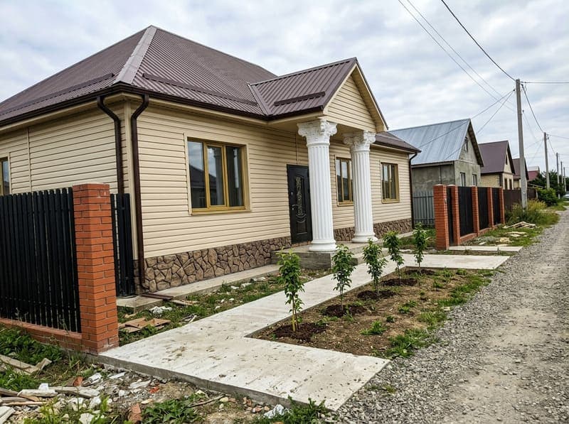 Дом с декоративными колоннами на сайдинге и поддельным камнем